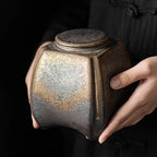 Person holding a textured ceramic jar against a black background